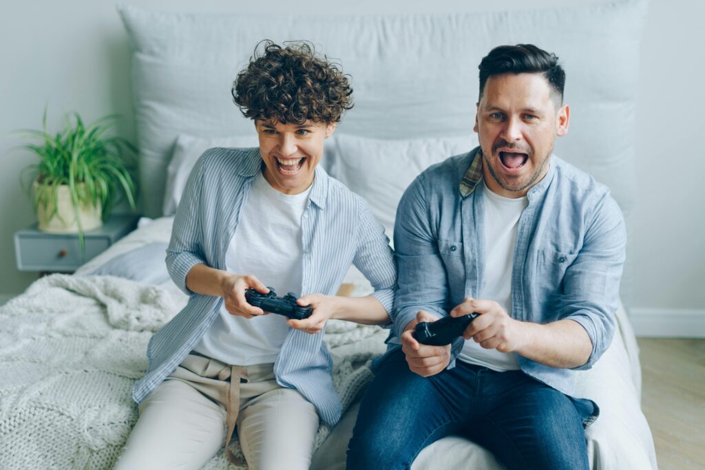 A couple having fun playing video games on a bed, showcasing enjoyment and connection.