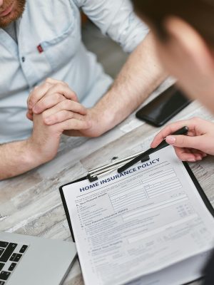 Two adults reviewing a home insurance policy document on a table with electronic devices.
