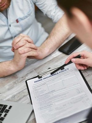 Two adults reviewing a home insurance policy document on a table with electronic devices.