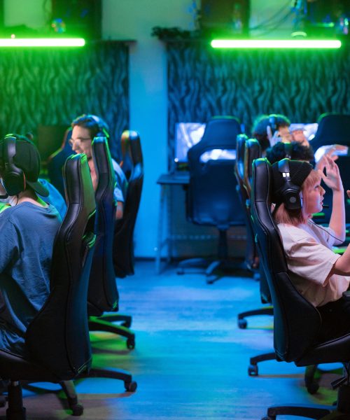 Group using computers at a gaming center with green lighting and headphones, teamwork concept.