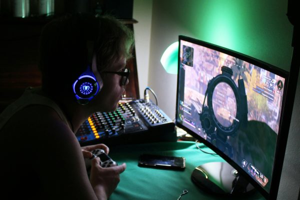 A dedicated gamer using a headset and controller while engrossed in a game, illuminated by green lights.