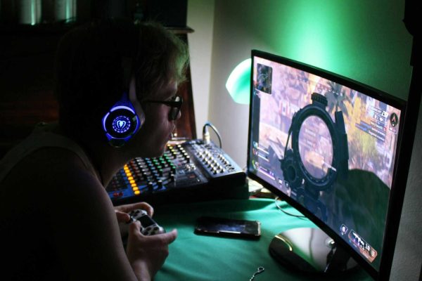 A dedicated gamer using a headset and controller while engrossed in a game, illuminated by green lights.